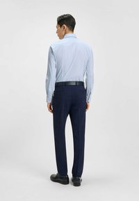 Camisetta azzurra chiara a maniche lunghe con motivo, abbinata a pantaloni blu navy. L'outfit presenta una cintura nera e scarpe nere lucide.