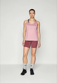 Débardeur de sport rose clair avec des accents noirs, associé à un short bordeaux et des chaussettes de sport grises. Des chaussures de gym noires complètent la tenue.
