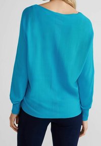 Turkos tröja med lös båturringning och långa ärmar. Tyget är slätt med en subtil textur längs bakre söm.
