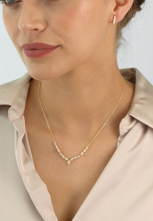 Gold-tone chain necklace with clear gemstones in marquise and round shapes. Worn with a silky light-colored blouse. Subtle earrings complement.
