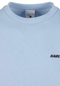 Gaiši zils džemperis ar ribotu apkakli, mīkstu tekstūru un melnu "KARL" logo priekšpusē.