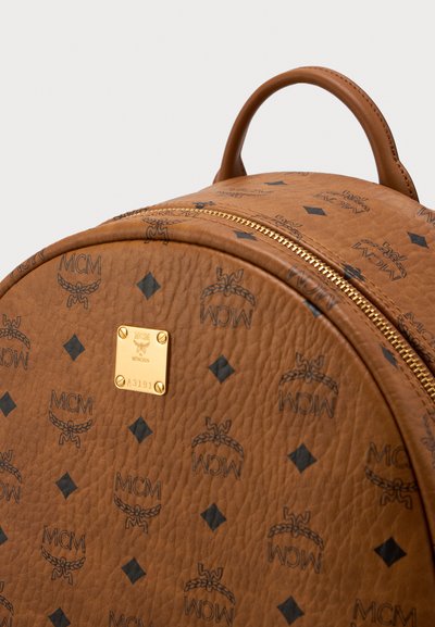 Brown leather MCM backpack with black logo print, gold zipper, and gold brand emblem plate on front panel.