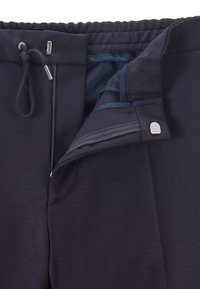 Tmavě modré kalhoty s elastickým pasem, šňůrkou, zapínáním na zip a knoflíkovým uzávěrem, ukazující vnitřní podšívku.