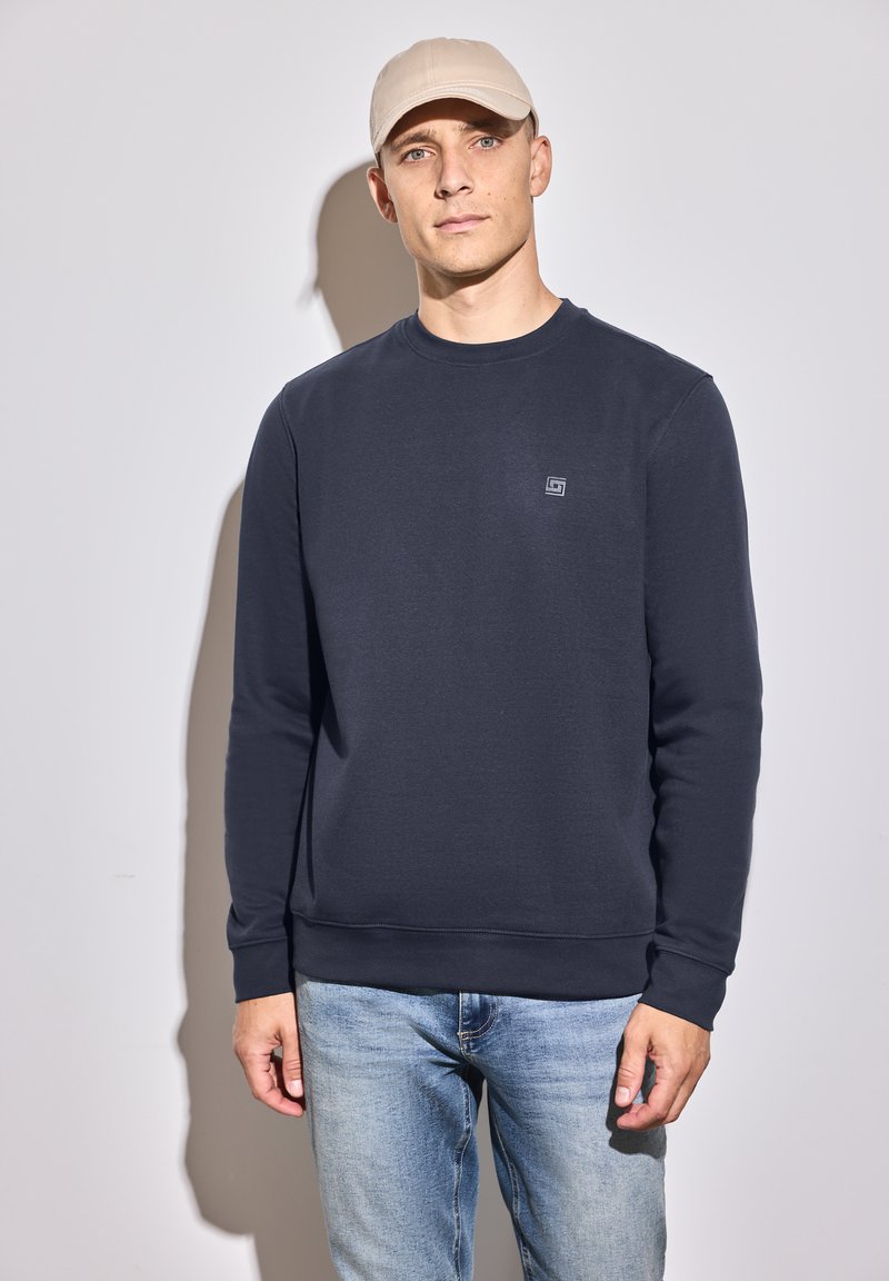 Navy blue sweatshirt made of cotton blend, featuring a crew neckline and ribbed cuffs. Paired with light blue denim jeans.