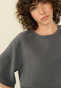 Haut à manches courtes gris foncé en tissu lisse et texturé. Dispose d'un col rond et de détails de couture subtils.