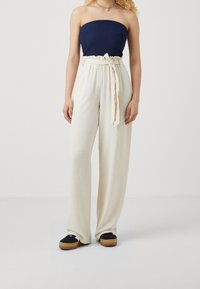 Pantalon blanc taille haute à jambes larges avec ceinture en tissu, associé à un haut bleu foncé sans bretelles et des chaussures à plateforme noires.