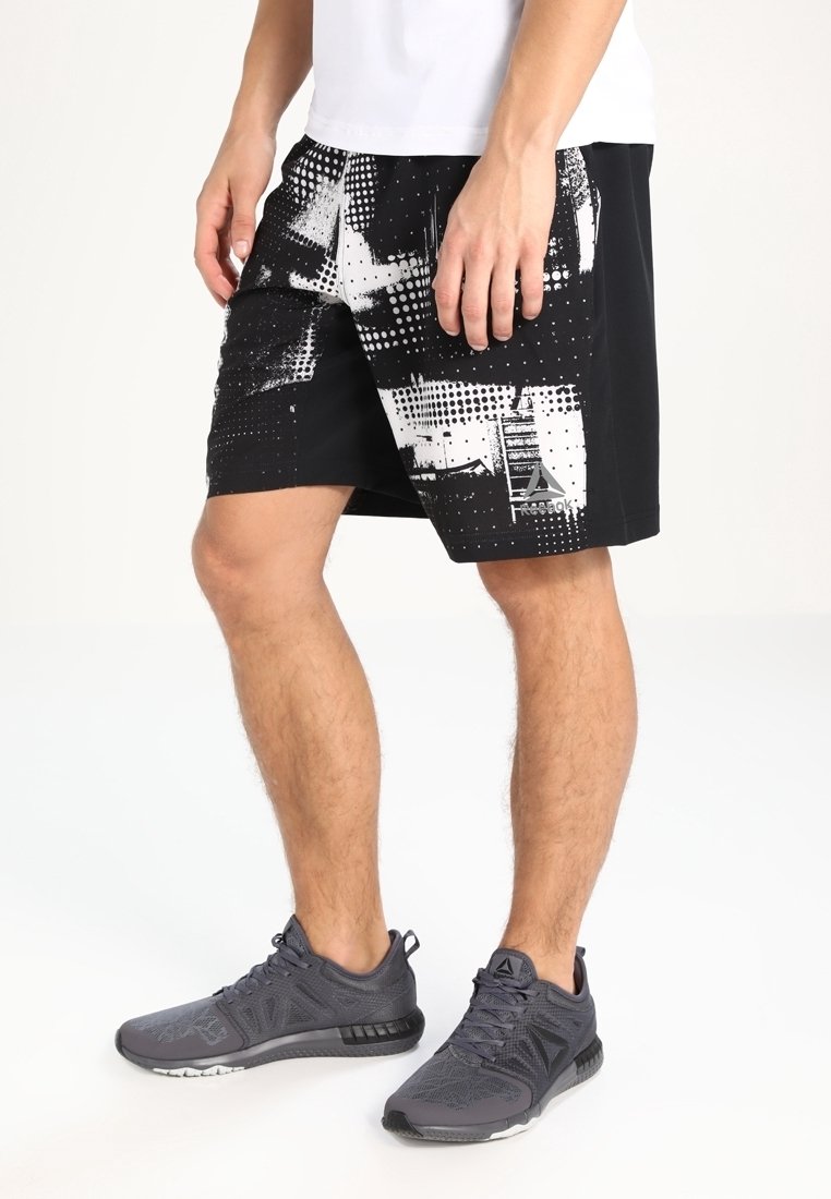 Schwarze Sportshorts mit einem geometrischen, monochromen Muster, das eine glatte Textur und seitliche Taschen aufweist. Dazu werden graue Sportschuhe getragen.