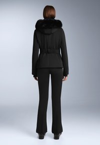 Crni vanjski kaput s kragnom od umjetnog krzna, strukiran, i suknjom koja se širi. Sadrži jaknu s užom remenom i detaljima na patentnim zatvaračima na hlačama.