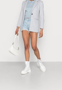 Long blazer gris clair sur un pull court bleu, assorti à un short en denim déchiré. Sac à main blanc et bottines blanches épaisses à lacets.