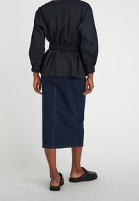 Černá texturovaná blůza s elastickým pasem, spárovaná s tmavě modrou džínovou midi sukni a černými botami na slip-on, pohled zezadu.