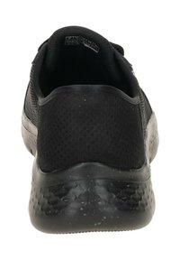 Scarpa atletica nera con superiore in rete traspirante e suola in gomma testurizzata con un design maculato. Vista posteriore, che mostra la forma del tallone arrotondato.