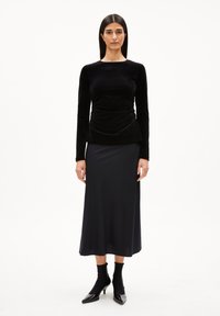 Zwarte fluwelen top met lange mouwen en gather taille, gecombineerd met een lange donkere rok. Gekenmerkt door zwart, nauwsluitend enkelschoeisel met puntige neuzen.