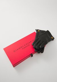 Gants en cuir noir avec des coutures texturées et des accents de boutons dorés, reposant sur une boîte rouge étiquetée "GIANNI CHIARINI FIRENZE."
