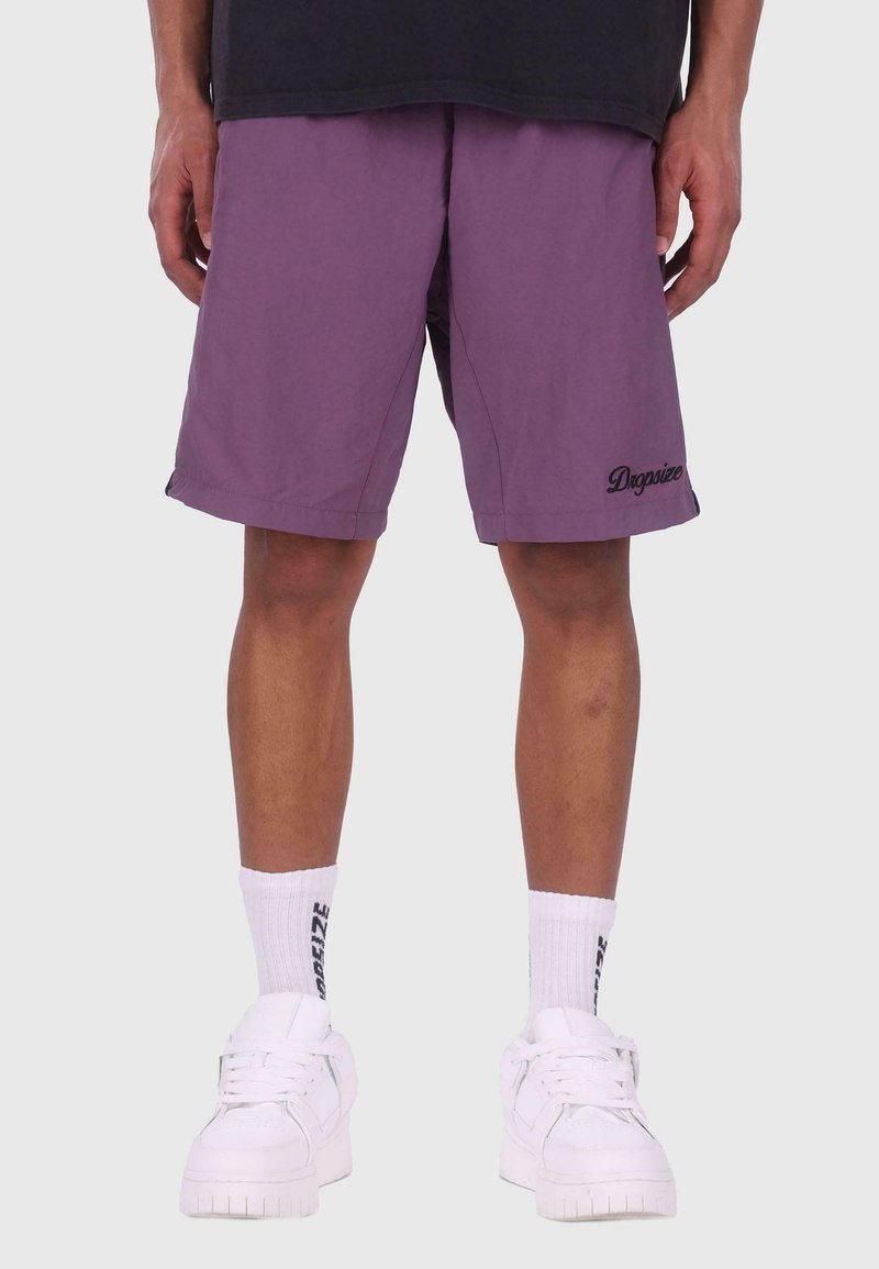 Pantalones cortos morados con detalle de logotipo negro, hechos de un tejido ligero. Calcetines blancos y zapatillas gruesas blancas completan el conjunto.