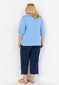 Világoskék pulóver, rövid puffujjakkal, sötétkék cropped nadrággal párosítva. Bézs, szőtt szandálokkal viselve. Simaság jellemzi az anyag textúráját.