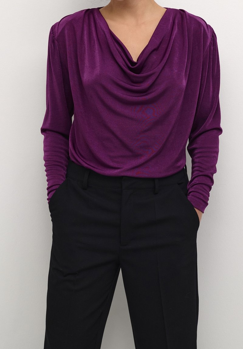 Haut col bénitier violet en tissu doux, à manches longues et design drapé, associé à un pantalon noir sur mesure.