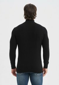 Pull en maille noir à col roulé avec des manches longues et un ourlet côtelé, porté de dos sur un jean bleu, mettant en avant l'ajustement près du corps.