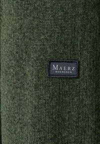 Dunkelgrüner Strickstoff mit strukturierter Oberfläche. Verfügt über ein kleines schwarzes Etikett mit weißem Text, auf dem "Maerz Muenchen" steht, das angenäht ist.