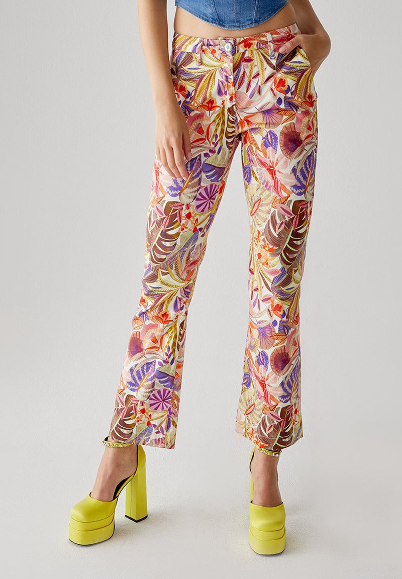 Pantaloni a vita alta con motivo floreale, dai colori vivaci e dal design aderente, realizzati in tessuto leggero; abbinati a scarpe con plateau gialle.