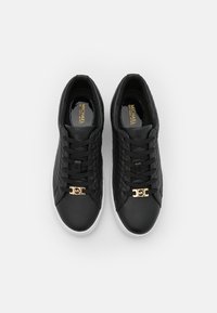 Ein Paar schwarze, gesteppten Sneakers mit weißen Sohlen, schwarzen Schnürsenkeln und goldfarbenem "MK"-Logo-Detail auf der Vorderseite, von oben gezeigt.