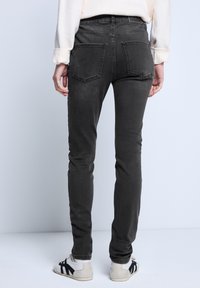 Dopasowane, ciemnoszare dżinsy o gładkiej teksturze; posiadają tylne kieszenie i przeszycia, w połączeniu z białymi i czarnymi butami sportowymi.