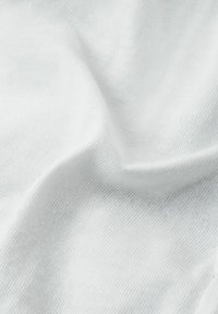 Biała bawełniana tkanina o miękkiej, gładkiej fakturze i widocznym wzorze splotu, delikatnie układająca się z subtelnym odbiciem światła.