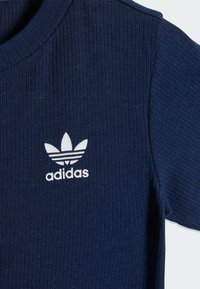 Tmavomodré rebrované tričko s okrúhlym výstrihom a krátkymi rukávmi. Na hrudi biely logo Adidas. Mäkká, textúrovaná tkanina.