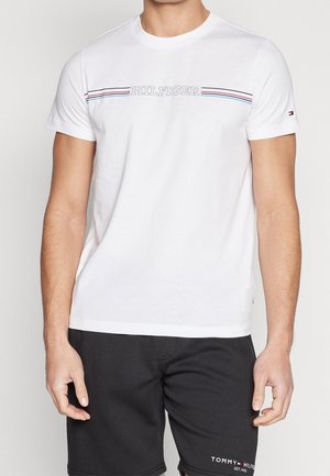 T-shirt en coton blanc avec un col rond, des manches courtes et un logo rayé rouge, blanc et bleu sur la poitrine.