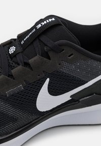 Crne i sive atletske tenisice s teksturiranim mrežastim gornjim dijelom, bijelim Nike Swoosh logom, podstavljenim ovratnikom i izraženim cik-cak akcentima sa strane.