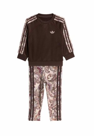 Haut Adidas marron à manches longues avec des rayures à motifs sur les manches, associé à des leggings imprimés paisley avec des rayures marron assorties.