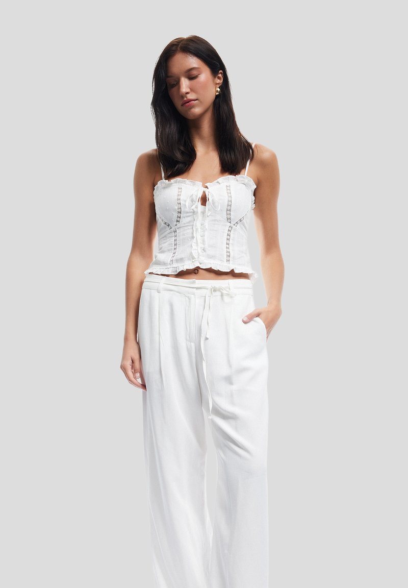 Crop top bianco in lino con rifiniture a volant e dettagli in pizzo, abbinato a pantaloni bianchi larghi con vita elastica e coulisse.