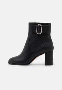 Bottine en cuir noir avec un bout arrondi, une surface texturée et un accent décoratif avec boucle. Dispose d'un talon haut épais pour la stabilité.