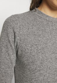 Maglione grigio lavorato a maglia con scollatura rotonda, caratterizzato da un motivo testurizzato e una vestibilità aderente. Il tessuto sembra morbido e leggermente melangiato.