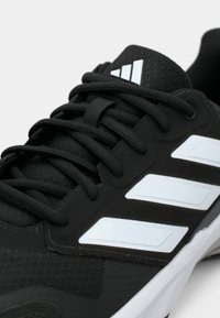 Čierna športová obuv s textúrovanou tkaninou a syntetickými vrstvami; obsahuje tri biele pruhy, čierne šnúrky a polstrovaný golier.