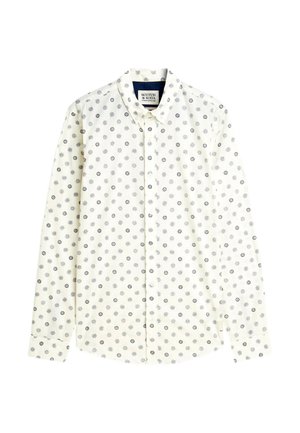 Chemise blanche à manches longues boutonnée avec petits motifs noirs de soleil et cercles, col pointu et étiquette de marque visible à l'intérieur du col.