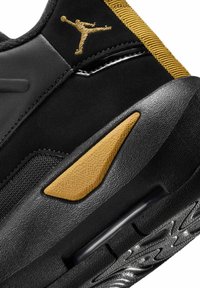 Zbliżenie na piętę czarno-złotego buta sportowego z teksturowaną podeszwą, amortyzacją powietrzną oraz złotym logo Jumpman na czarnej cholewce.