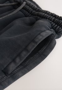 Pantalon en tissu noir avec une taille élastique et une poche latérale visible sur un fond clair.