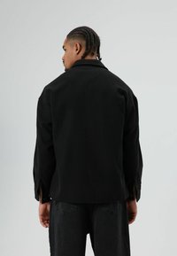 Zwarte jas met kraag en een losse pasvorm. Gemaakt van zacht stof, voorzien van zijsplitten en een eenvoudig, onopgesmukt ontwerp.