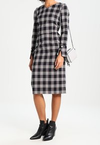 Svart och vit rutig figurnära klänning med långa ärmar, rundad halsringning, sidfickor och knappdetaljer, kombinerad med svarta ankle boots.