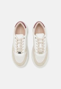 Baskets blanches et beiges avec une boîte à orteils perforée, des accents en daim beige clair, un onglet de talon bordeaux et le logo Calvin Klein sur la languette.