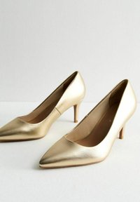 Guld höga klackar med spetstoppdesign, slät metallisk finish och smala klackar. Inuti finns en mjuk foder.