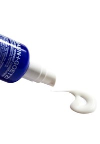 Blaue Quetschflasche mit weißem Pumpkopf, der eine glatte weiße Creme auf einem weißen Hintergrund ausgibt. Text und Logo sind auf der Flasche sichtbar.