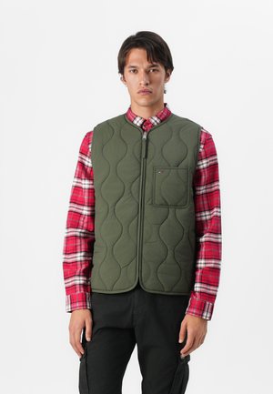 Olive green quilted vest with a rounded neckline, front zip closure, and a chest pocket, layered over a red plaid shirt.