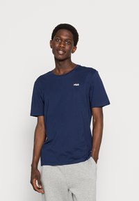 Camiseta de algodón azul marino de manga corta y cuello redondo. Presenta un pequeño logo de FILA en rojo y blanco en el lado izquierdo del pecho. Suitable para uso casual.