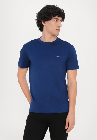 Tamsiai mėlynos spalvos trumpomis rankovėmis marškinėliai su apvali kaklo iškirpte, pagaminti iš lygaus audinio, su mažai logotipu viršutinėje krūtinės dalyje.