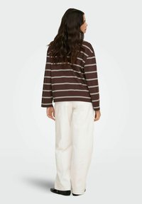 Pruun triibuline triiksärk pika varrukaga, valgete joontega, valmistatud pehmest kangast. Sobitatud lahtiste valgete pükstega ja mustade kingadega. Vaade tagant.