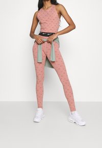 Rosa ärmlös topp med cirkulära mönster och matchande tights, som har en svart midja. Lager på lager med en ljusgrön topp knuten i midjan.