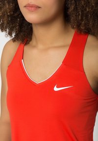Rode Nike tanktop met een V-hals, dunne banden en witte logodetail. Beschikt over een gladde, aansluitende pasvorm die geschikt is voor sportkleding.
