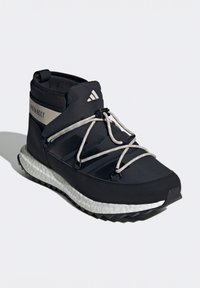 Černá atletická bota s texturovaným svrškem, elastickými tkaničkami a bílou polstrovanou podrážkou. Obsahuje logo Adidas a štítek "MOON BOOT".