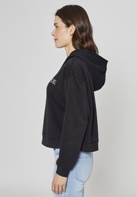 Sweat à capuche noir coupé, manches longues et capuche avec cordon ; présente un texte graphique à l'avant. Tissu texturé ; poignets et ourlet côtelés.